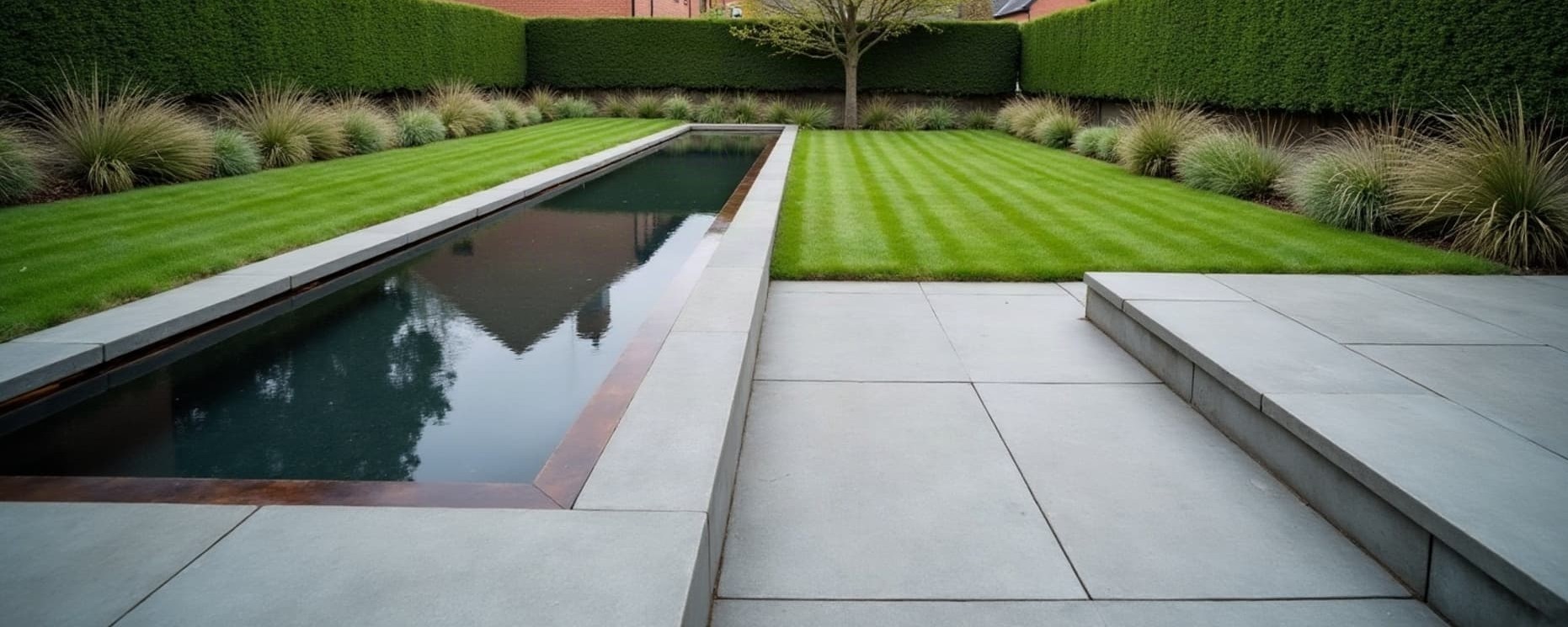 Jardin de particulier terminé : terrasse en pierre bleue, bassin miroir à rive corten, pelouse tondue et haie taillée